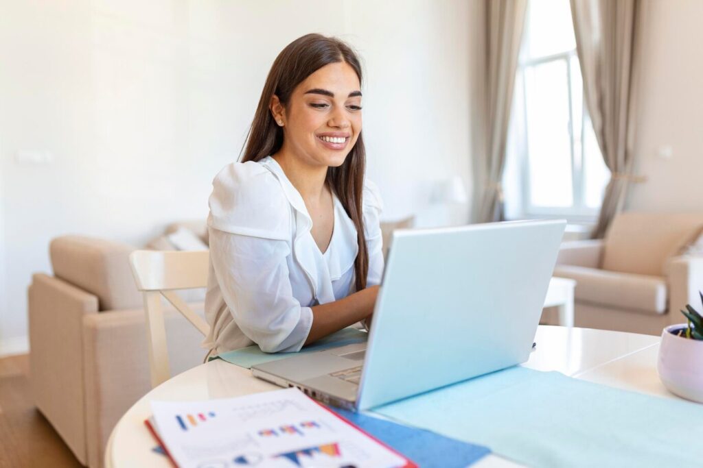 person with long hair sitting at a table, working on a laptop
