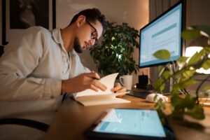 person seated at a desk, writing in a notebook