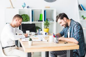 people work collaboratively at a wooden table filled with colorful pens