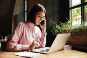 woman in a pink shirt works on a laptop at a wooden desk