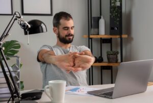 person stretches their arms while seated at a desk with a laptop