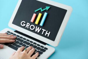 Hands typing on a laptop displaying a "GROWTH" graphic with upward arrows on a blue background.