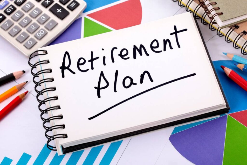 Notebook with "Retirement Plan" written on it, surrounded by colored pencils, a calculator, and charts on a desk.