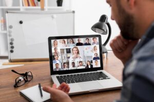 Man on a video call with diverse colleagues displayed on his laptop screen in a home office.