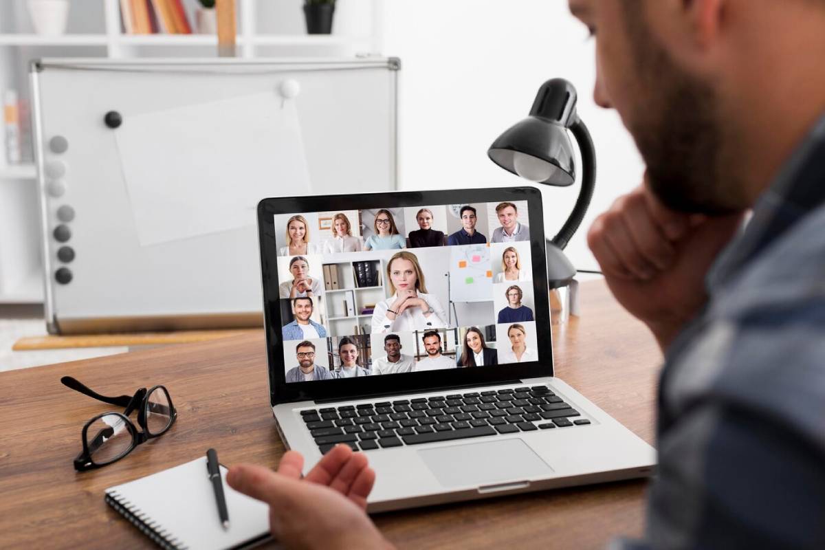 Man on a video call with diverse colleagues displayed on his laptop screen in a home office.