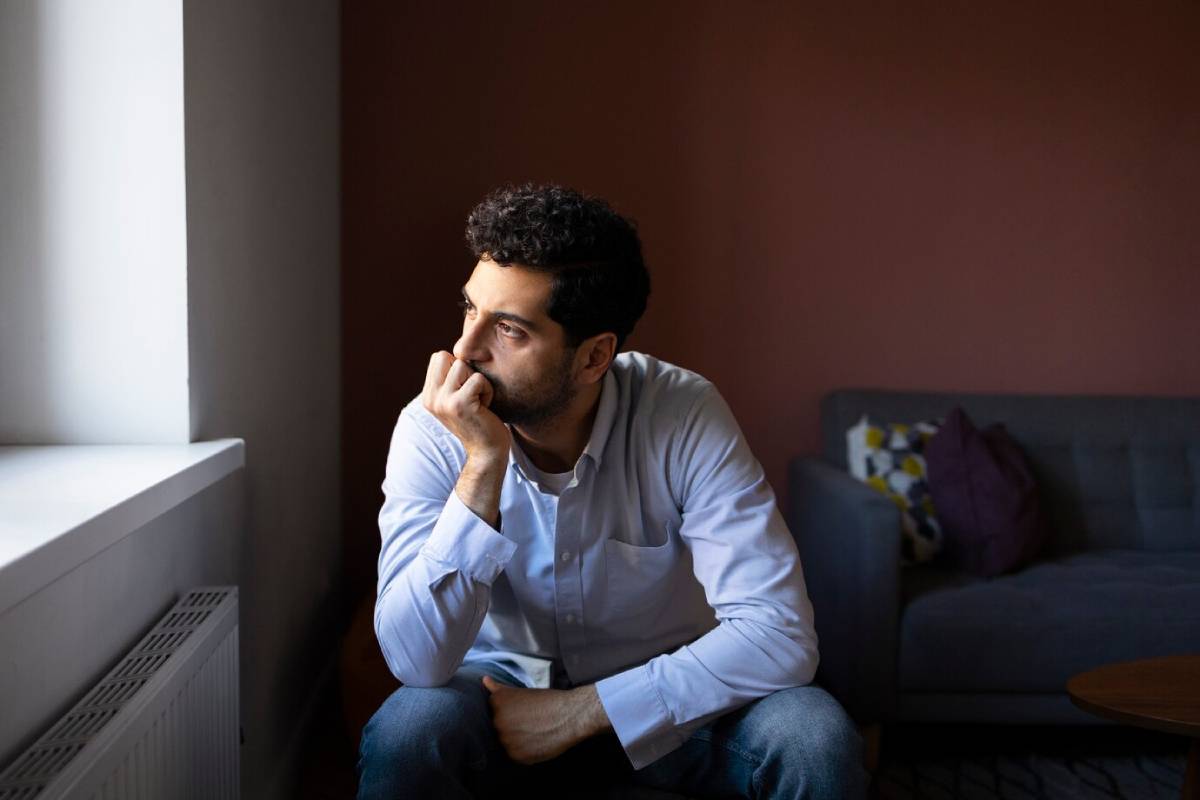  Man sitting near a window, lost in thought, in a softly lit room.