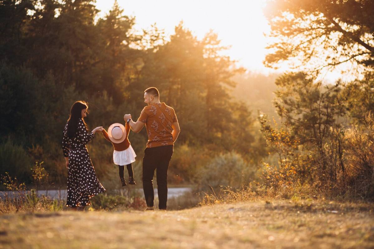 Family playing with young child in a sunlit forest at sunset.