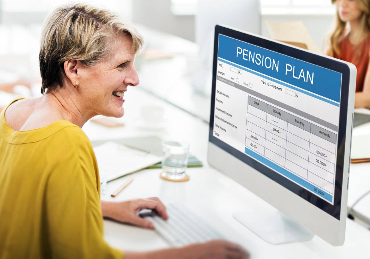 Elderly woman smiling while viewing a pension plan on a computer screen in an office setting. 