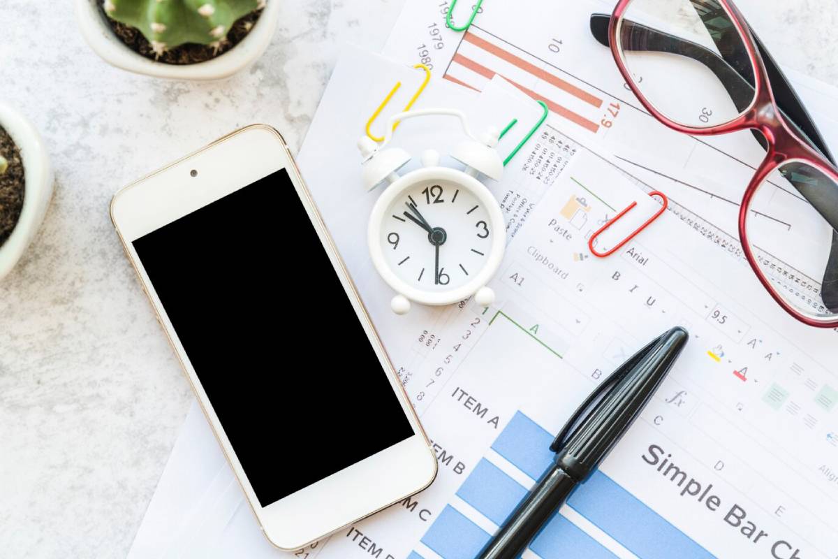 Work desk with smartphone, alarm clock, glasses, and documents with charts.