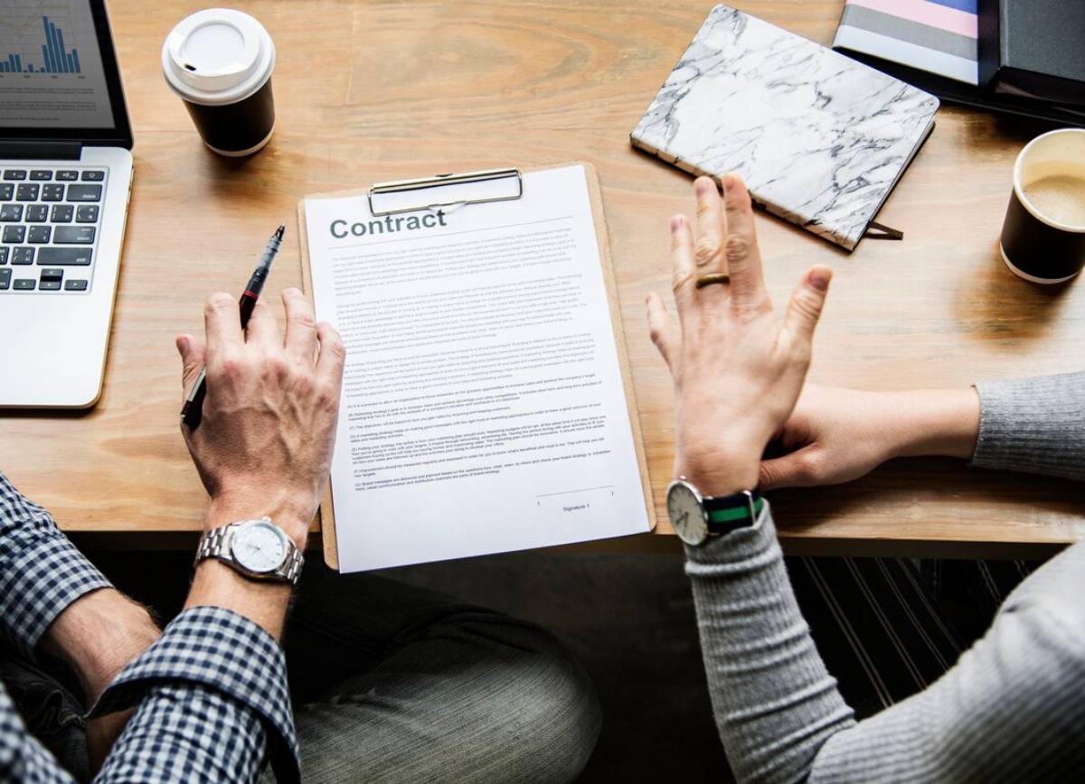  Two people reviewing a contract on a table with laptops and coffee cups in background.