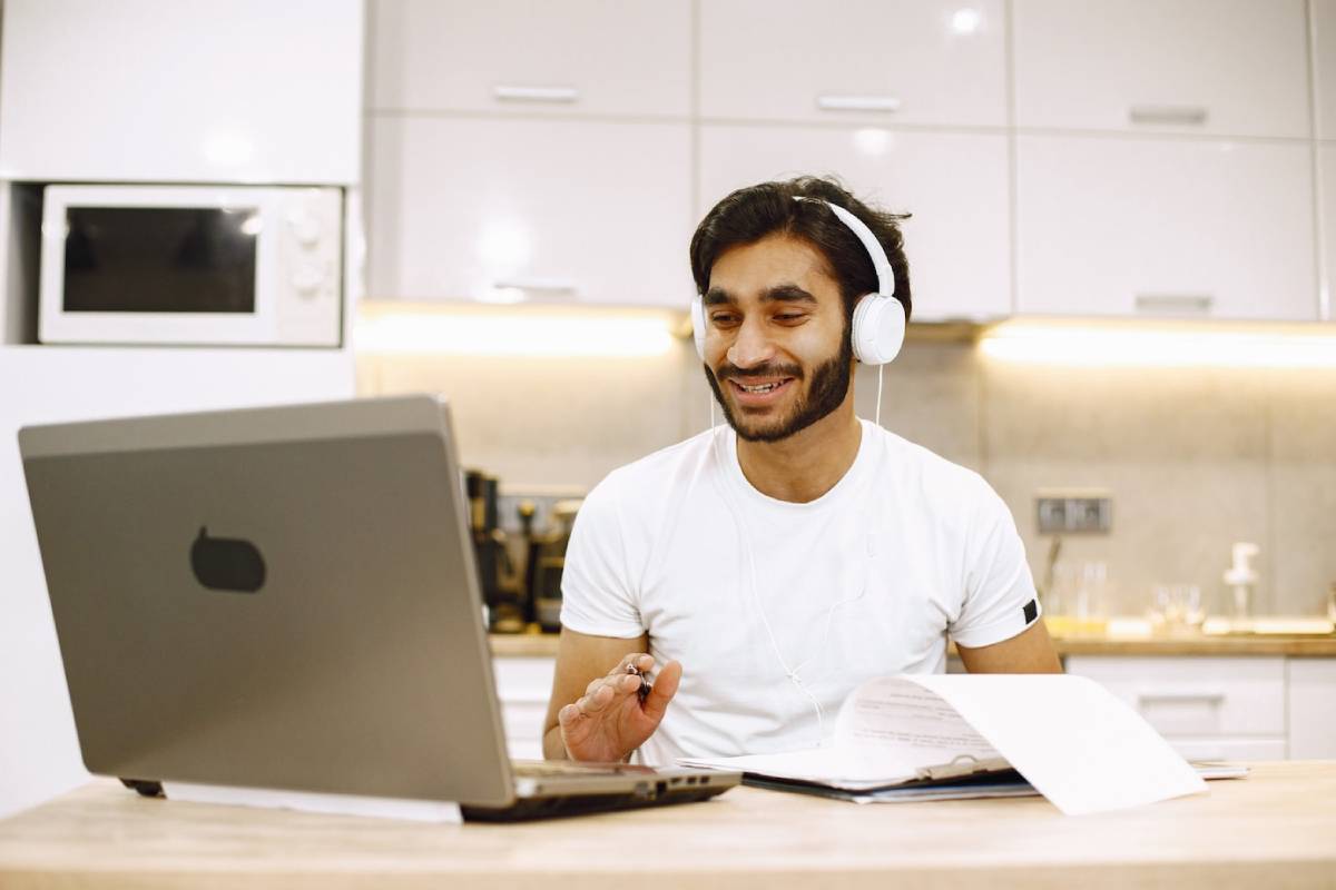 Man with headphones smiling at laptop in a modern kitchen.